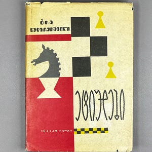 May include: Vintage book cover with a chess theme. The design features a black knight, a red and white checkered pattern, and yellow pawn illustrations. The cover has text in a foreign language.