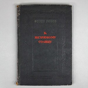 May include: A vintage book with a black cover featuring the title "K nezrimomu solntsu" in red lettering. The author's name, "Boris Rozov," is printed at the top. The book has a worn appearance, suggesting age and use.