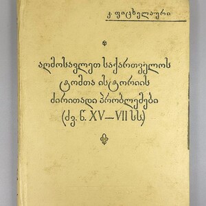 May include: A vintage book with a light tan cover. The cover features text in a unique script, with the title and author's name prominently displayed. The book's overall aesthetic suggests it is an older publication, possibly a historical text.