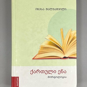 May include: A hardcover book with a light green cover featuring an open book illustration. The book's title, in Georgian script, is displayed prominently. The cover also includes the author's name and the word "Morphology".