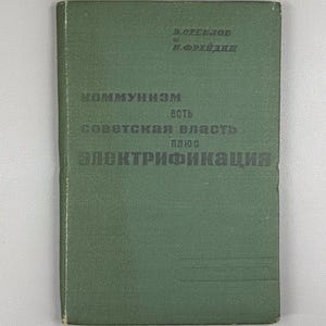 Può includere: Un libro d'epoca con copertina verde. Il titolo, in russo, recita: "Il comunismo è il potere sovietico più l'elettrificazione". I nomi degli autori sono stampati in alto. Il libro mostra segni di usura.