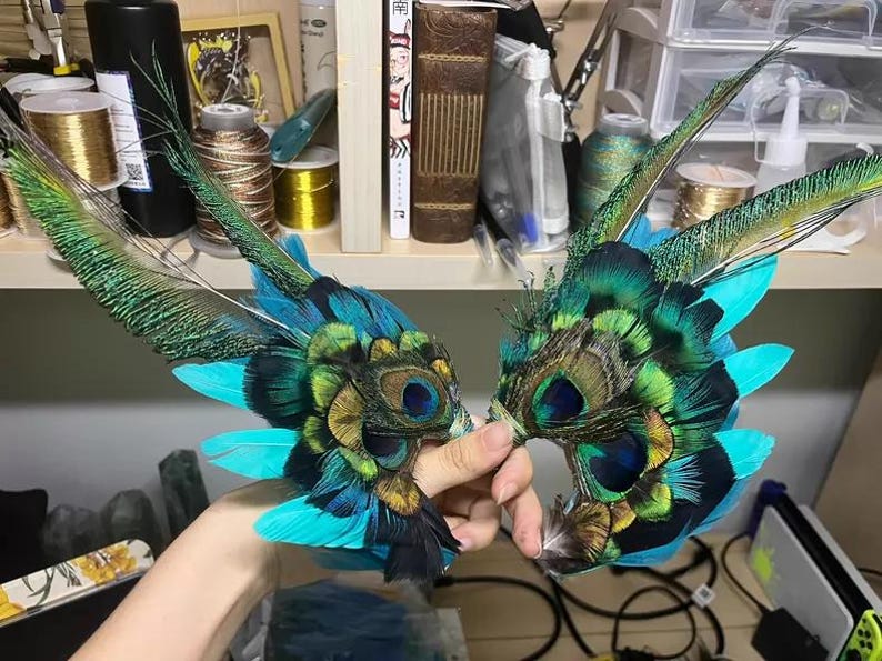 Puede incluir: Un par de m&aacute;scaras para los ojos hechas con plumas de pavo real. Las m&aacute;scaras presentan plumas de color turquesa, verde y negro, con detalles intrincados alrededor de las cuencas de los ojos. Dise&ntilde;adas para disfraces o decoraci&oacute;n.