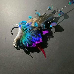 May include: A vibrant ear cuff featuring a peacock feather design. The cuff showcases a spectrum of colors, including teal, blue, purple, and red, with a silver-tone metal ear wrap. The feathers are arranged to create a striking, artistic accessory.