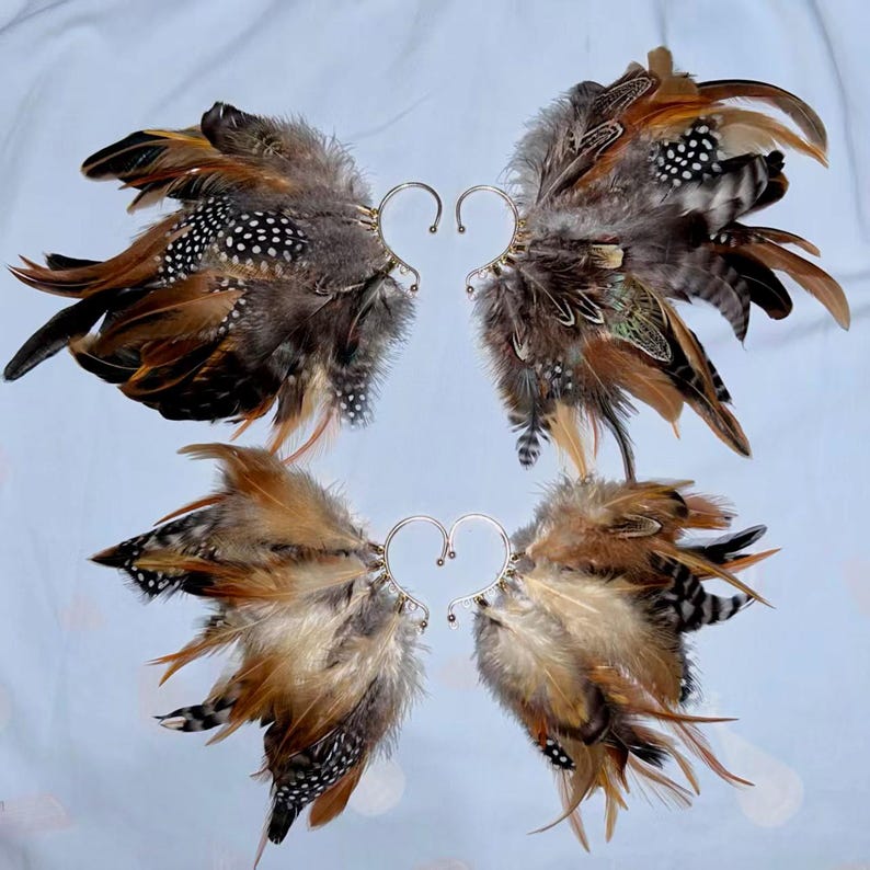 May include: Four pairs of feather ear cuffs. Each cuff features a heart-shaped wire design and is adorned with brown, black, and white speckled feathers. The feathers are arranged to resemble wings, creating a unique accessory.