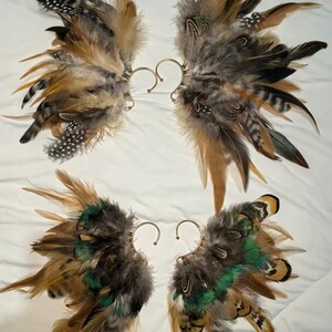 May include: Four pairs of feather ear cuffs. Each cuff features a cluster of brown, tan, black, and green feathers attached to a gold-colored ear wire. The feathers vary in size and texture, creating a layered effect.