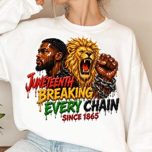 Puede incluir: Sudadera blanca con un diseño gráfico. El diseño incluye el texto "Juneteenth Breaking Every Chain Since 1865", un retrato de un hombre, un león rugiendo y un puño cerrado con cadenas.