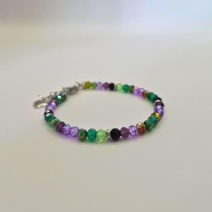 Peut inclure: Un bracelet de perles avec un mélange de perles à facettes colorées dans des tons de violet, de vert et de couleurs irisées. Le bracelet a une chaîne et un fermoir argentés, avec un petit charme en forme de cœur. Les perles mesurent environ 0,5 cm de diamètre.