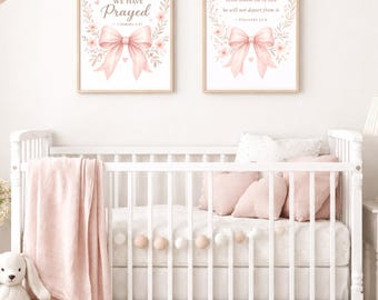 May include: Two rectangular wall art prints in light wood frames featuring pink floral wreaths and bows. The left print reads, For This Child We Have Prayed, 1 Samuel 1:27. The right print reads, Train up a child in the way he should go.
