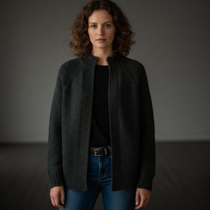 May include: A dark grey cardigan with a ribbed collar and open front. The cardigan is worn over a black top and blue jeans. A brown belt with a silver buckle is visible. The outfit is simple and classic.