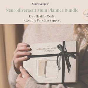 May include: A Neurodivergent Mom Planner Bundle is held in the image. The box is tied with a dark ribbon. The text on the box reads "ADHD Brain + Nutrition Planner". The bundle includes "Easy Healthy Meals" and "Executive Function Support".