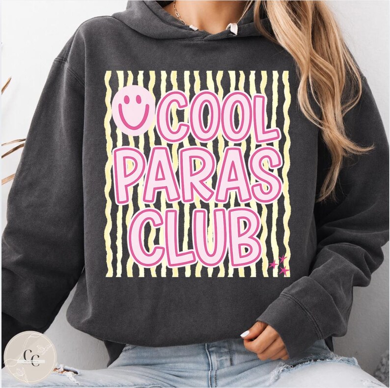 May include: Dark gray hoodie with the text "COOL PARAS CLUB" in pink, outlined in white, and a smiley face. The text is set against a background of black and yellow vertical stripes. The hoodie has a drawstring hood and long sleeves.