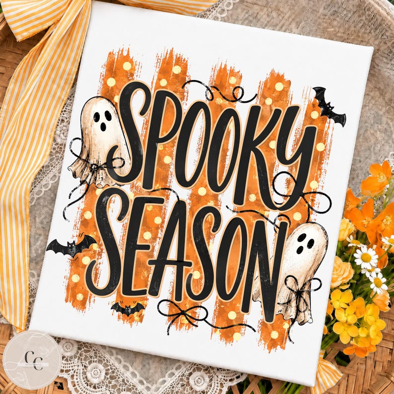May include: A rectangular white canvas print featuring the black text "SPOOKY SEASON" in a stylised font. The design includes orange brushstroke stripes with yellow dots, two white ghost illustrations with black bows, and three small black bats.
