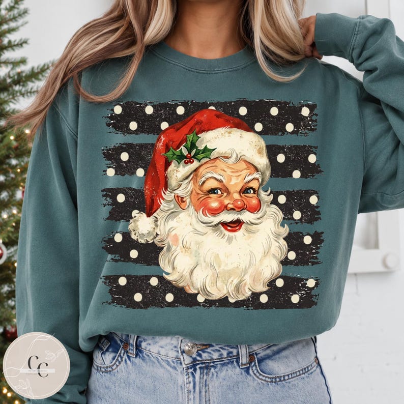 May include: A teal long-sleeve sweatshirt featuring a graphic of a vintage-style Santa Claus face with a red hat and holly sprig. The background of the graphic consists of horizontal black distressed stripes with white polka dots throughout.