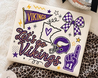 May include: A white t-shirt featuring purple and yellow graphics including a Vikings pennant, a Minnesota state outline with a heart, a checkered bow, a football helmet, and a foam finger with the text Let's go Vikings and #1.