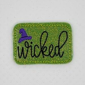 May include: Green glitter iron-on patch with a purple witch hat and the word "wicked" in black cursive.