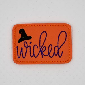 May include: Orange felt patch with a black witch hat and purple embroidered text that says "wicked".
