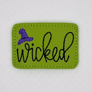 May include: A rectangular, lime green patch with the word "wicked" in black script. A purple witch hat is embroidered above the word. The patch has a stitched border.