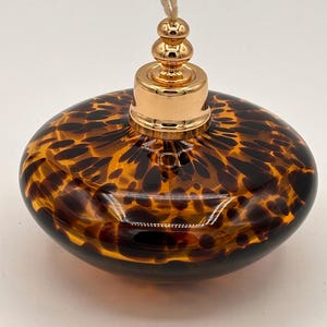 Puede incluir: Lámpara de aceite ovalada decorativa con un patrón de carey en tonos marrón y ámbar. Cuenta con una tapa de metal dorado y una mecha. El diseño evoca la decoración vintage, ideal para la decoración del hogar.