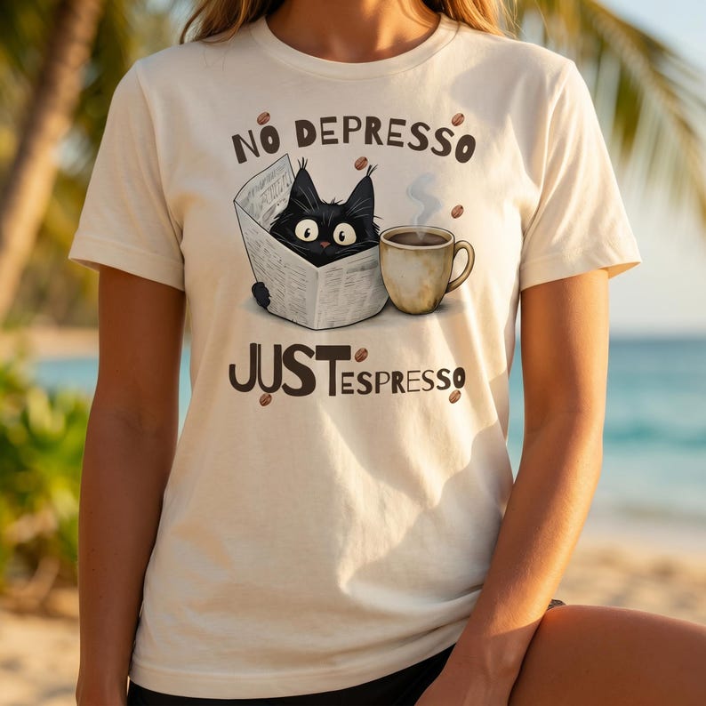 May include: Cream-colored t-shirt with a graphic of a black cat reading a newspaper next to a steaming coffee cup. The text on the shirt reads "No Depresso Just Espresso" in brown lettering, with coffee beans scattered around.