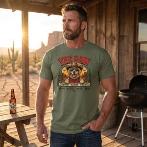 K&ouml;nnte beinhalten: Olivgr&uuml;nes T-Shirt mit einem Aufdruck eines Hundes mit Cowboyhut und Halstuch, der Text "Yee Paw" ist dar&uuml;ber. Das Shirt hat auch den Text "Good Times - Cold Drinks - No Bad Days". Eine Flasche Craft-Bier steht auf einem Holztisch.