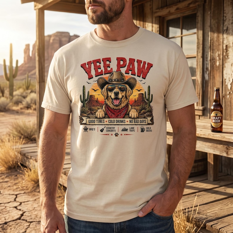 K&ouml;nnte beinhalten: Beiges T-Shirt mit einem Aufdruck, der einen Hund mit Cowboyhut und Sonnenbrille zeigt, dem Text "Yee Paw" und dem Satz "Good Times Cold Drinks No Bad Days". Das Shirt hat auch Symbole f&uuml;r BBQ's, Country-Konzerte, Ausfl&uuml;ge zum See und kaltes Bier.