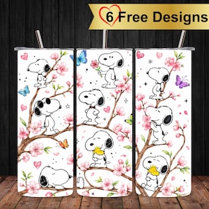 Puede incluir: Un vaso cilíndrico blanco con un patrón repetitivo de personajes de Snoopy, flores de cerezo rosas y mariposas coloridas. El diseño incluye pequeños corazones rosas y detalles de estrellas. Una pajita de metal está insertada en la tapa.