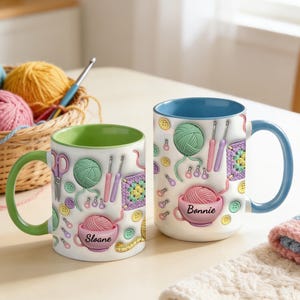 Peut inclure: Deux tasses en céramique blanche avec un motif coloré de pelotes de laine, crochets, ciseaux, boutons et carrés granny. Une tasse a un intérieur et une anse verts avec le nom Sloane, l'autre un intérieur et une anse bleus avec le nom Bonnie.