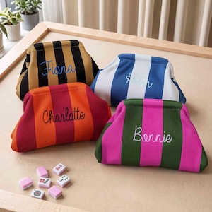 May include: Four striped pouches with kiss-lock closures, each embroidered with a name. One is black and tan with 'Fiona', one blue and white with 'Helen', one orange and red with 'Charlotte', and one green and pink with 'Bonnie'.