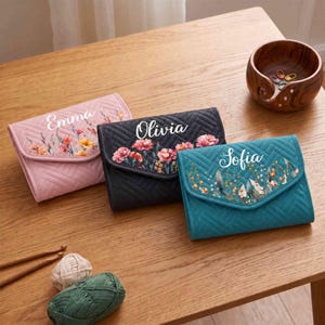 May include: Three quilted wallets in light pink, black, and teal, each featuring a floral print and a white name printed on the flap. The names Emma, Olivia, and Sofia are displayed on the respective wallets. The wallets have a chevron pattern.