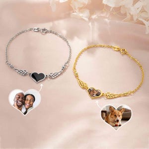 Könnte beinhalten: Ein silberfarbenes Kettenarmband mit einem herzförmigen Anhänger, der Engelsflügel und eine schwarze Einlage aufweist, sowie ein goldfarbenes Kettenarmband mit einem herzförmigen Anhänger, Engelsflügeln und einem individuellen Hundefoto.