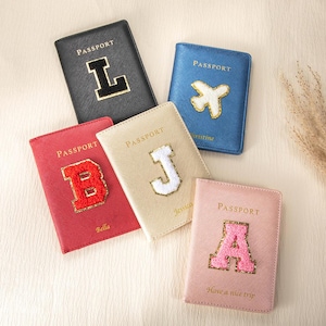 May include: Five rectangular passport holders in black, blue, red, gold, and pink. Each features the word PASSPORT, a large letter or airplane patch, and some include names like Bella, Jessica, and Christine or the text Have a nice trip.