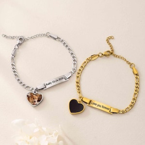 Pode incluir: Duas pulseiras de corrente de metal com fechos lagosta. A pulseira prateada apresenta um pingente de coração com a foto de um cão e uma barra retangular gravada com Buddy 02-14-2026. A pulseira dourada tem um coração preto e Love you forever.
