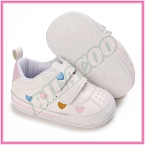 May include: White baby sneakers with embroidered hearts in blue, pink, and gold. The shoes have a pink accent on the heel and a velcro strap closure. The soles are white and textured.