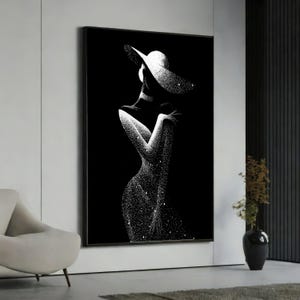 Può includere: Una stampa artistica da parete incorniciata che presenta un'illustrazione in bianco e nero ad alto contrasto di una figura che indossa un cappello a tesa larga. La figura è resa con una texture punteggiata e scintillante su sfondo nero.