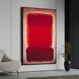Pode incluir: Grande pintura abstrata com moldura preta. A obra apresenta um esquema de cores vermelho vibrante com uma borda vermelha mais clara. A pintura é exibida em uma parede branca, com uma cadeira moderna e um vaso preto na sala.