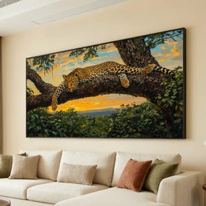 May include: A large framed canvas art print shows a leopard resting on a tree branch. The leopard has a spotted coat, set against a sunset sky and green foliage. The artwork is displayed above a cream-coloured sofa.