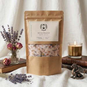 Könnte beinhalten: Ein brauner Papiersack mit "Mood Reader" Badesalzen mit einem transparenten Fenster, das Lavendel- und Orangenbotanik zeigt. Eine brennende Kerze in einem goldfarbenen Halter, ein kleines Glas mit getrockneten Blumen und eine dekorative Drachenstatue.