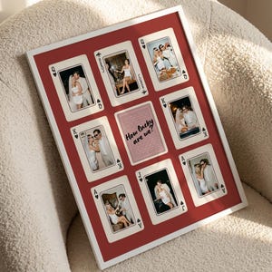 May include: A rectangular white-framed wall art piece featuring a red background with eight playing card designs and a central card back graphic. Each card displays a photograph of a couple. The center card features the text How lucky are we?