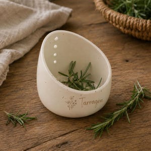 May include: A cream-colored ceramic herb bowl with a slanted rim and three small drainage holes near the top. The exterior features a delicate line drawing of wildflowers and the word Tarragon printed in a simple, elegant script font.