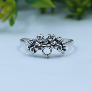 Sterling silver cherub ring featuring two angel figures holding a heart motif in a delicate openwork design.