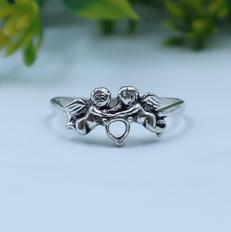 Sterling silver cherub ring featuring two angel figures holding a heart motif in a delicate openwork design.