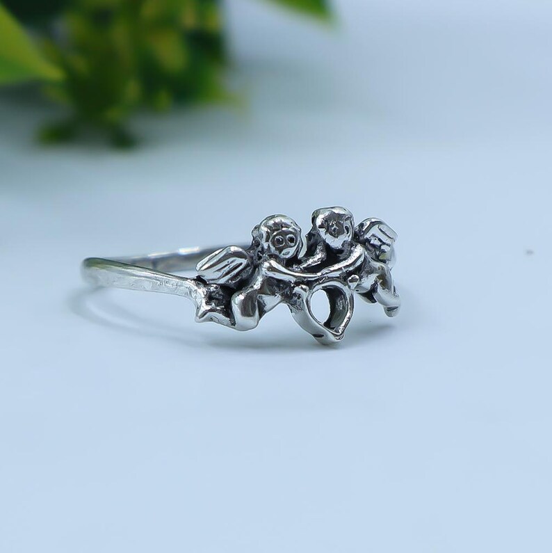 Side profile of a vintage-inspired angel ring showcasing detailed wings, sculpted cherubs, and a slim silver band.