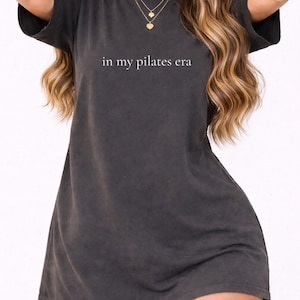 Puede incluir: Una taza de cerámica blanca con un asa negra y el texto "But First, Coffee" en un estilo manuscrito. La taza está sobre una superficie blanca. La taza mide aproximadamente 10 cm de alto.