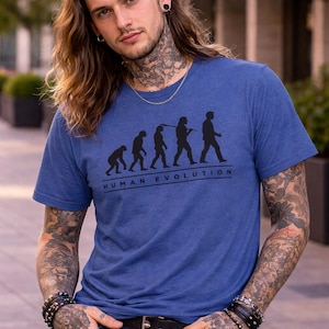 Pode incluir: Camiseta azul com um gráfico preto da evolução humana. O texto "HUMAN EVOLUTION" está impresso abaixo. A camiseta tem mangas curtas e gola redonda.
