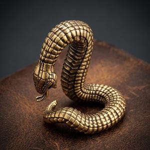 Può includere: Statuetta di serpente in ottone dettagliata con corpo strutturato e squamoso e lingua biforcuta. Il serpente è arrotolato in una posa suggestiva, che mostra il suo design intricato. Oggetto decorativo.