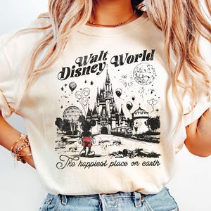 Puede incluir: Camiseta de color marfil con un gr&aacute;fico en blanco y negro de Walt Disney World. El dise&ntilde;o incluye el castillo, Mickey Mouse, globos y fuegos artificiales, con el texto "Walt Disney World" y "The happiest place on earth."