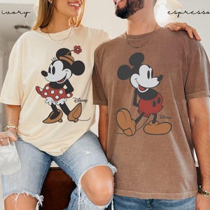 Puede incluir: Dos camisetas, una marfil y otra espresso, con Mickey y Minnie Mouse. La camiseta marfil tiene a Minnie Mouse con un vestido de lunares rojos. La camiseta espresso tiene a Mickey Mouse con pantalones cortos rojos. Ambas camisetas tienen el logo de Disney.
