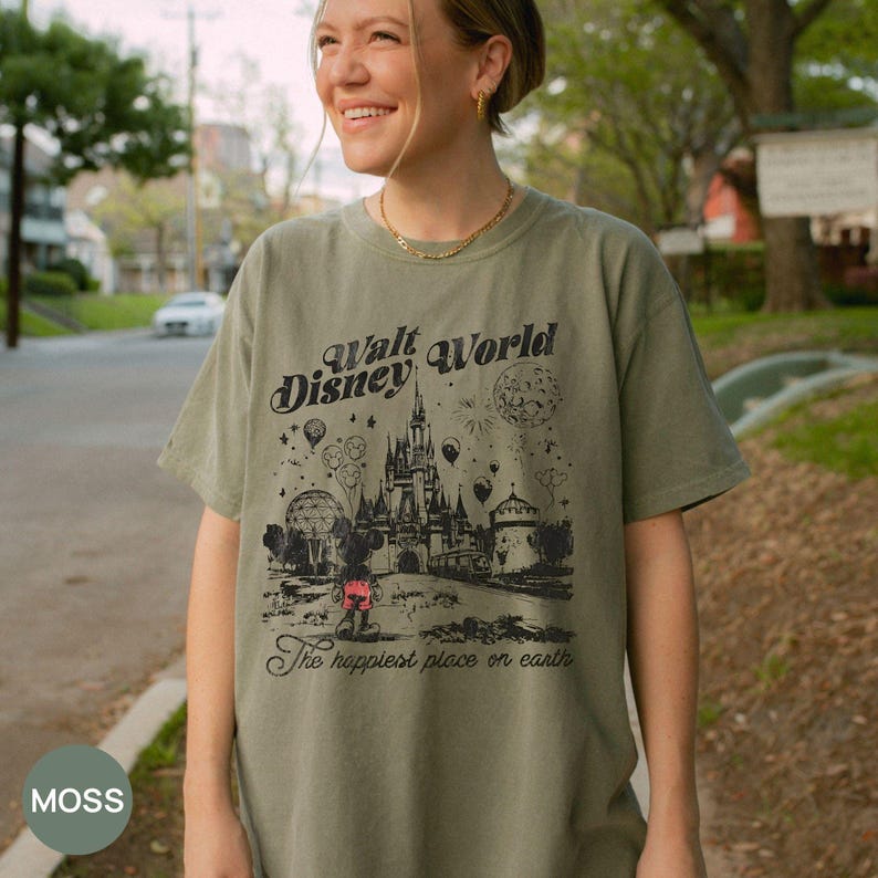 Puede incluir: Camiseta verde musgo con un gr&aacute;fico negro del castillo de Walt Disney World, Mickey Mouse y el texto "Walt Disney World" y "The happiest place on earth". La camiseta es de corte holgado.
