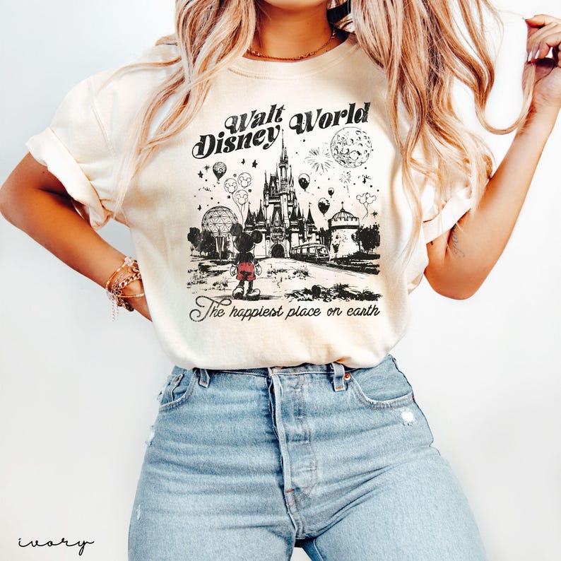 Puede incluir: Camiseta de color marfil con un gr&aacute;fico en blanco y negro de Walt Disney World. El dise&ntilde;o incluye el castillo, Mickey Mouse, globos y fuegos artificiales, con el texto "Walt Disney World" y "The happiest place on earth."
