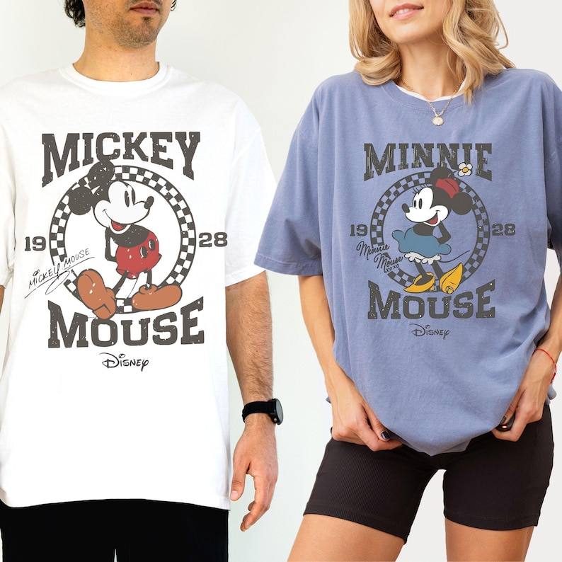 Puede incluir: Dos camisetas con Mickey y Minnie Mouse de Disney. La camiseta blanca tiene a Mickey Mouse en un c&iacute;rculo con el texto "Mickey Mouse 1928". La camiseta azul tiene a Minnie Mouse con el texto "Minnie Mouse 1928".